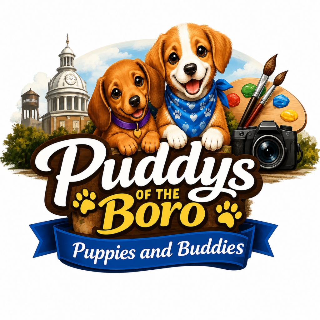 Illustrated logo for Puddys of the Boro: Puppies and Buddies featuring two cheerful cartoon puppies resting atop a rustic wooden sign. Behind them are recognizable Murfreesboro landmarks, including the Rutherford County Courthouse and the Murfreesboro water tower, set against a blue sky. To the right are an artist's paint palette with brushes and a camera, representing the project's combination of art and photography. The title "Puddys of the Boro" appears in large white and gold lettering with paw-print accents, while a blue ribbon below reads "Puppies and Buddies." The design conveys a warm, playful celebration of pets, creativity, and the Murfreesboro community.