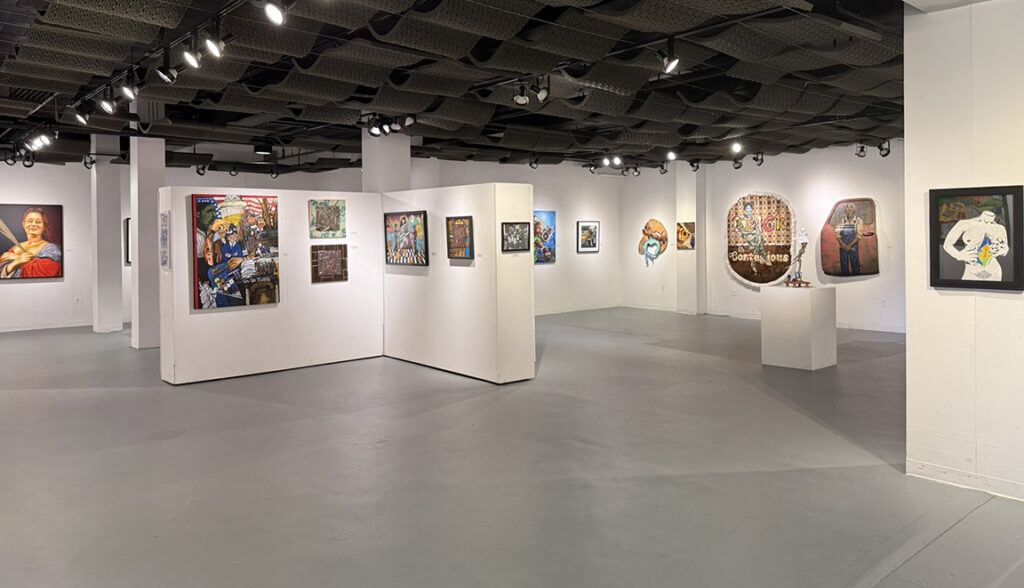 Gallery interior with white partition walls displaying a diverse selection of colorful paintings, mixed-media works, and sculpture beneath black track lighting.