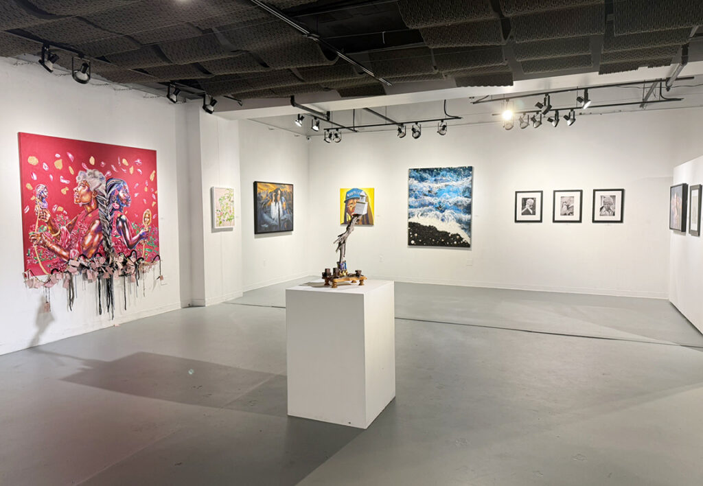 Wide gallery view featuring a large red mixed-media artwork, paintings, framed drawings, and a sculpture displayed on a white pedestal in the center of the space.