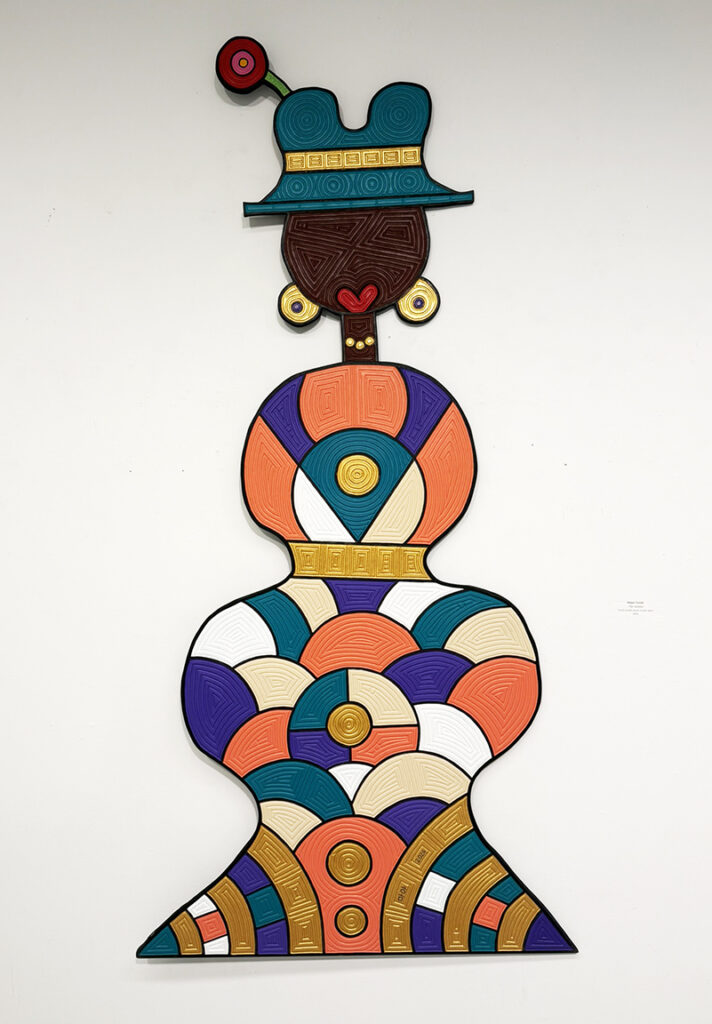 Colorful wall-mounted mixed-media figure composed of bold geometric patterns in teal, orange, purple, gold, cream, and brown, topped by an abstract headdress.
