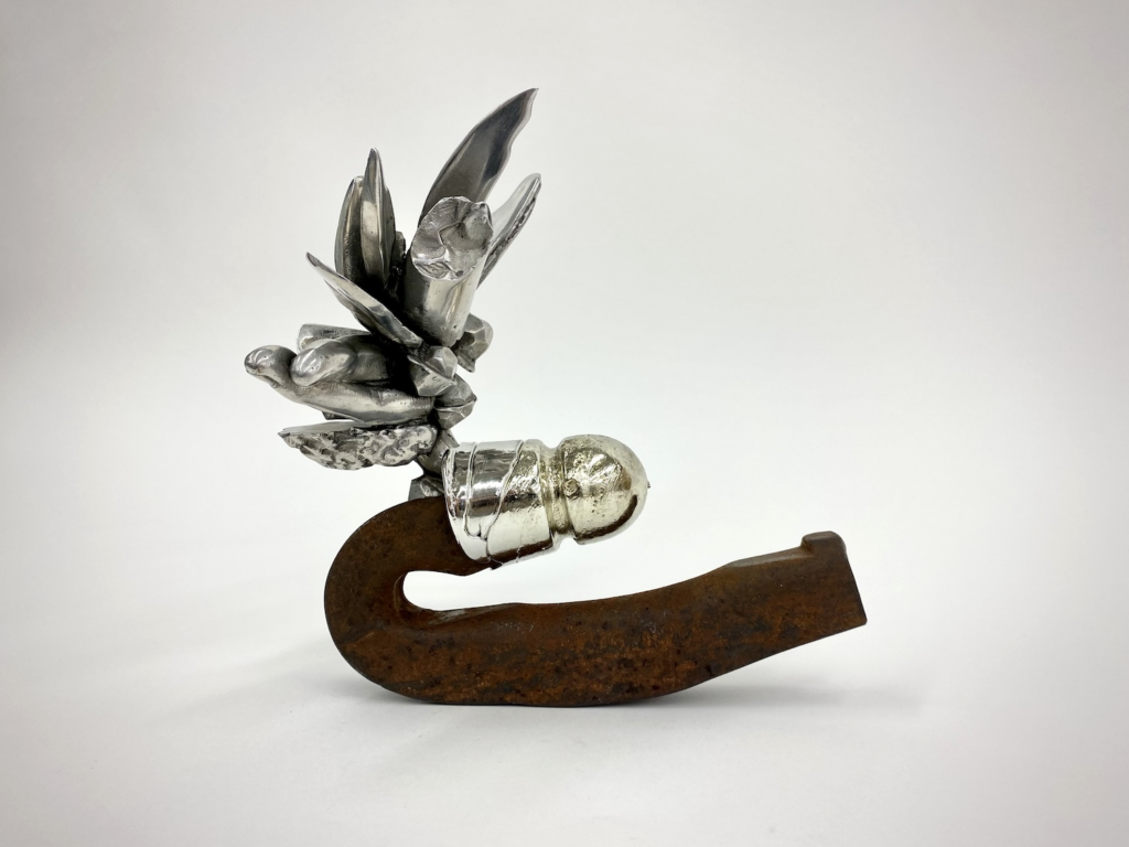 Emily Budd, Eureka Babe: Found-object assemblage featuring a rusted, curved metal base supporting a reflective silver form composed of a small figure and clustered leaflike shapes.
