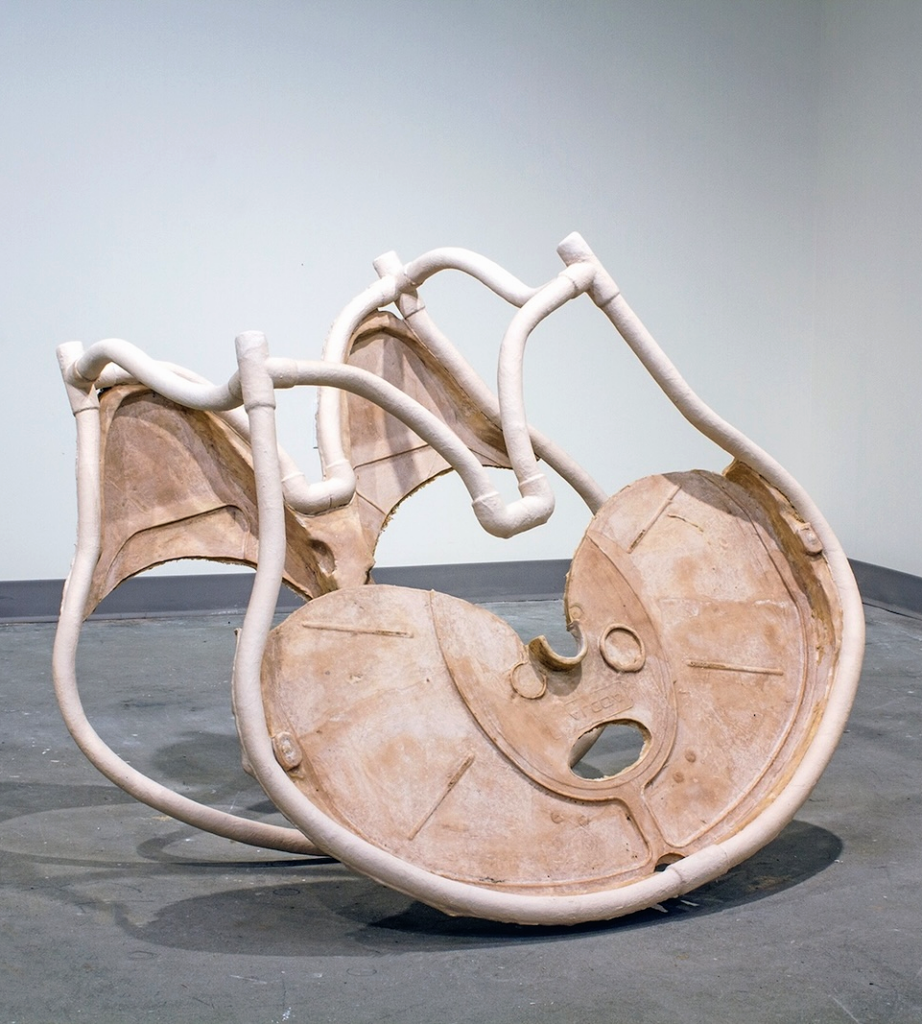 Jonathan Durham, Slicer: Large pale pink sculpture resembling overlapping circular blades or reels, connected and surrounded by looping tubular forms.