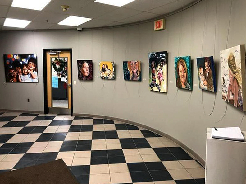 Interior view of Murfree Art Gallery featuring a curved gray wall lined with colorful figurative paintings by MTSU Art and Design students and area artists, displayed above a black-and-white checkered floor.