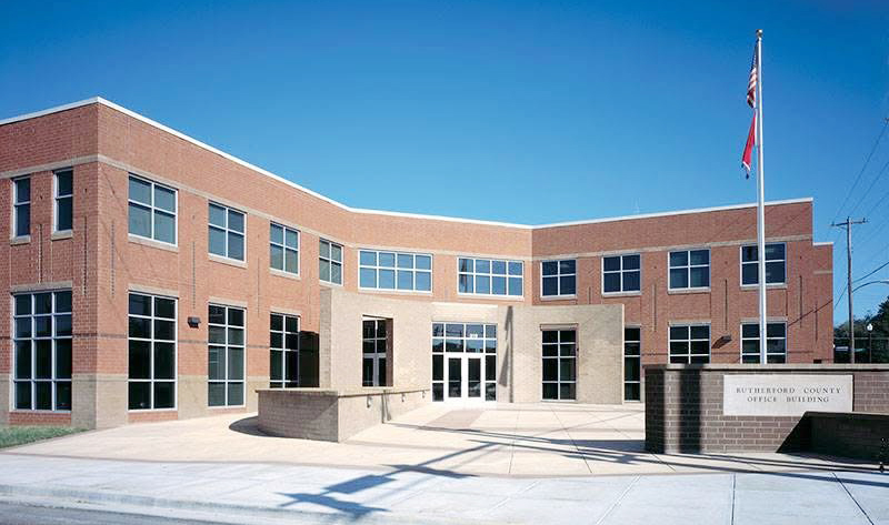 Rutherford County Office Building: Exterior view of the two-story brick Rutherford County Office Building, home of Murfree Art Gallery, with a curved entrance plaza and flagpoles beneath a clear blue sky.